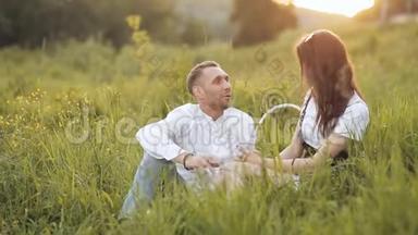 一对年轻夫妇坐在一片明亮的绿色草地上。 恋爱中的<strong>情侣</strong>。 微笑，在外面享受温暖的<strong>时光</strong>
